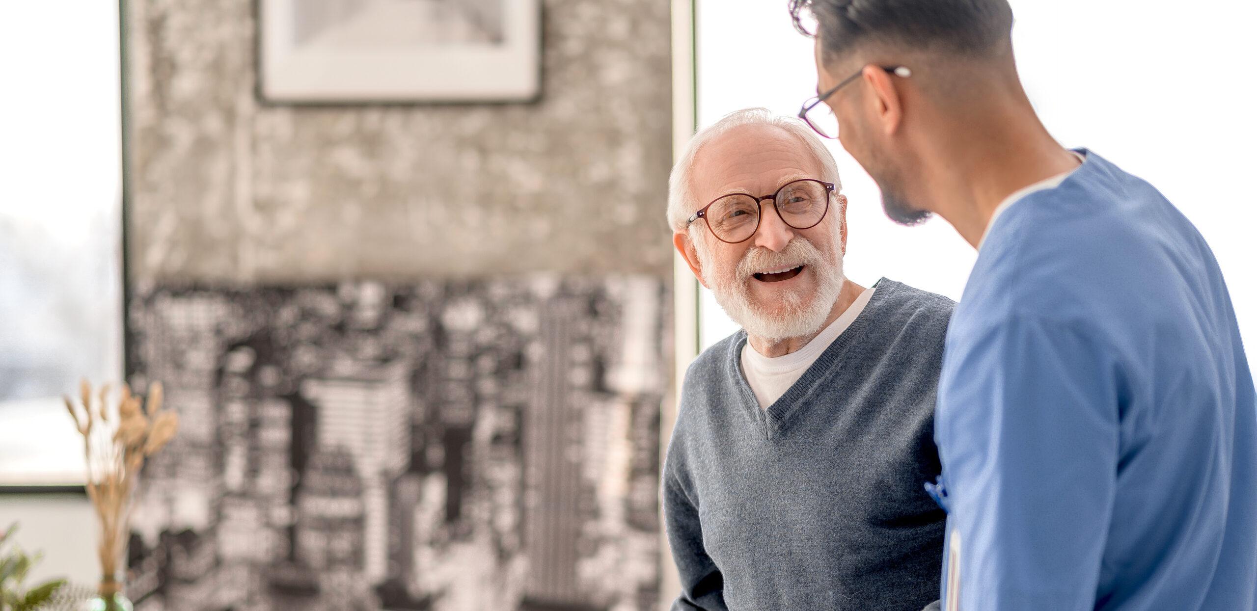 Old man standing by the table supported by a nurse
