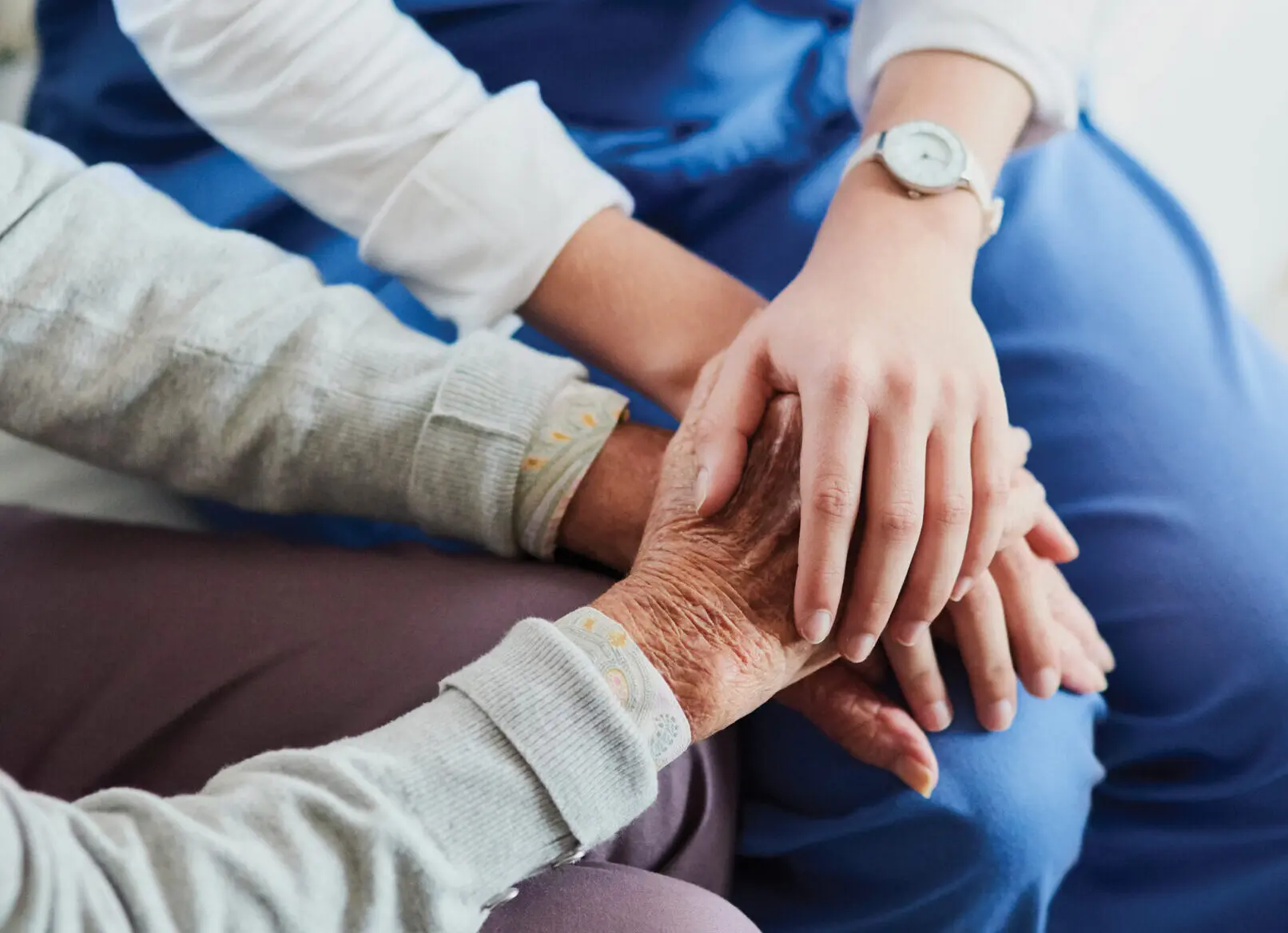 Healthcare provider holds a senior's hands with their faces out of the picture